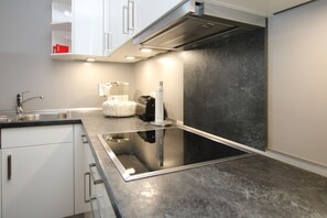 Eine moderne Küche mit einem schwarzen Induktionskochfeld, weißen Schränken und einer Edelstahl-Spüle.