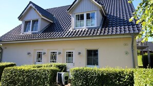 A two-story house with a tiled roof, multiple windows, and a well-maintained hedge in front. - Wiesenweg 4, Whg. 1, Wiesenkieker - Ferienwohnung mit 3- Zimmern auf ca. 76m² (Wyk auf Föhr)