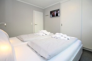 Une chambre d’hôtel avec deux lits, du linge de lit blanc, un téléviseur à écran plat fixé au mur et une porte dotée d’une poignée.