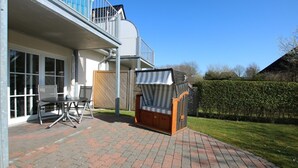 A patio with a table and chairs, a covered seating area, and a view of a building with a balcony. - Wiesenweg 4, Whg. 1, Wiesenkieker - Ferienwohnung mit 3- Zimmern auf ca. 76m² (Wyk auf Föhr)