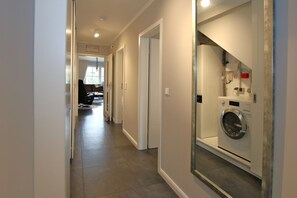 A hallway with a washing machine and a large mirror reflecting the room.