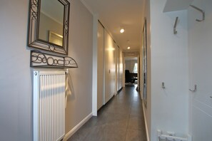 Un couloir étroit avec un radiateur, un miroir et une porte sur le côté droit.