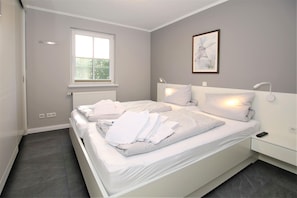 Quarto com uma cama grande, janela, radiador e um quadro na parede.