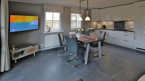 A modern kitchen with white cabinets, a dining area with a table and chairs, and a flat-screen TV mounted on the wall. - Wiesenweg 4, Whg. 1, Wiesenkieker - Ferienwohnung mit 3- Zimmern auf ca. 76m² (Wyk auf Föhr)