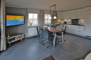 Une cuisine moderne avec des meubles blancs, un coin repas comprenant une table et des chaises, et un téléviseur à écran plat fixé au mur.