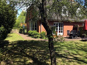 Een bakstenen huis met een terras en een overdekte zitplaats buiten, met een boom op de voorgrond.