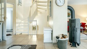 A modern living room with a staircase, a fireplace, and a clock on the wall. - Strandstraße 77a, Haus Nordseeluft - House half with 120m² over 3 floors (Wyk auf Föhr)