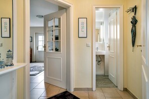 A hallway with a door leading to a bathroom, a rug on the floor, and framed pictures on the walls. - Strandstraße 77a, Haus Nordseeluft - House half with 120m² over 3 floors (Wyk auf Föhr)