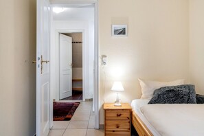 Hotelkamer met een bed, nachtkastje met een lamp, een klein nachtkastje met een lamp, een vloerkleed, een deur naar een badkamer en een lijst met een foto aan de muur.