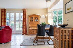 Een eethoek met een houten tafel, zwarte stoelen met bekleding, een rode bank en een houten kast.