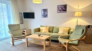 Un salon comprenant un canapé, deux fauteuils, une table basse, un téléviseur et une lampe.