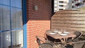 Une terrasse avec une table dressée pour quatre personnes, un mur en briques et une fenêtre à cadre bleu.