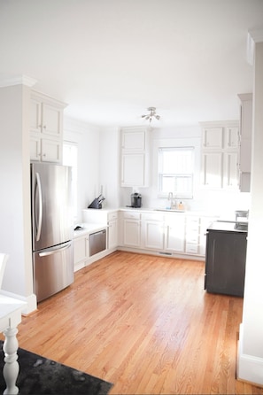 A modern kitchen with white cabinetry, stainless steel appliances, and a wooden floor.