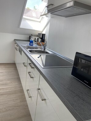 A modern kitchen with a built-in oven, a stainless steel sink, and a window above the countertop. - Apartment Mond 8002 - Sol y Mar - Apartment Mond - 8002 - "Sol y Mar" - (Dahme)