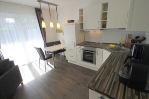 A modern kitchen with white cabinets, a built-in oven, a dining table with chairs, and pendant lights. - 1011 - Holiday apartment Strandgut - 1011 Holiday apartment Strandgut (Dahme)
