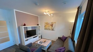 Una sala de estar con una televisión de pantalla plana, una mesa de centro, dos sofás y un cuadro en la pared.
