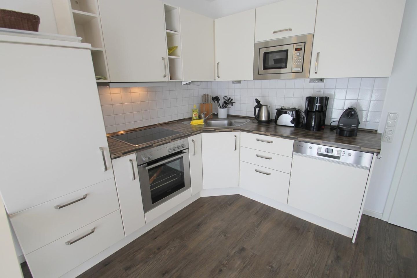 A modern kitchen with white cabinets, a built-in oven, a microwave, and a dishwasher.