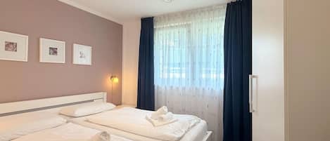 A hotel room with two beds, a bedside lamp, and a window with curtains.