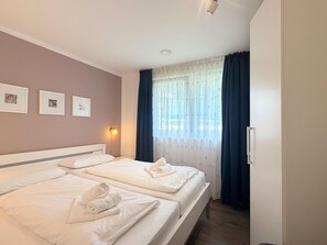 Quarto de hotel com duas camas, uma luminária de cabeceira e uma janela com cortinas.