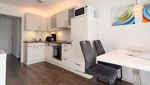 A modern kitchen with white cabinets, a built-in oven, and a dining area with a white table and two grey chairs. - 1010 - Seesternweg - OG - 1010 / Seesternweg in Dahme (Dahme)
