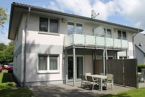 A two-story house with a balcony, a fenced patio, and a car parked in the driveway. - 1010 - Seesternweg - OG - 1010 / Seesternweg in Dahme (Dahme)