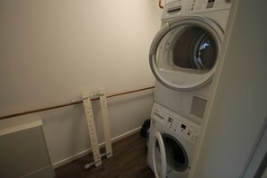 Une buanderie avec des machines à laver et des sèche-linge superposés, un plancher en bois et un mur blanc.