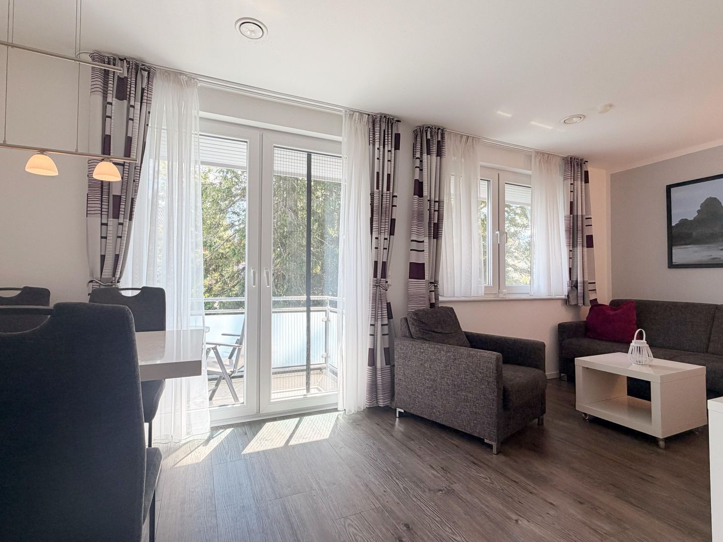 A modern living room with a sofa, a dining table with chairs, and a balcony with curtains.