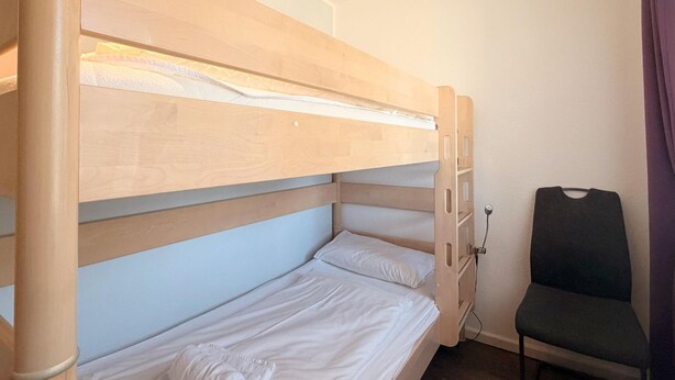 A bunk bed with a wooden frame and white bedding, a chair, and a power outlet on the wall. - 1010 - Seesternweg - OG - 1010 / Seesternweg in Dahme (Dahme)