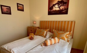 A double bed with striped bedding, a nightstand with a lamp, and two framed pictures on the wall.