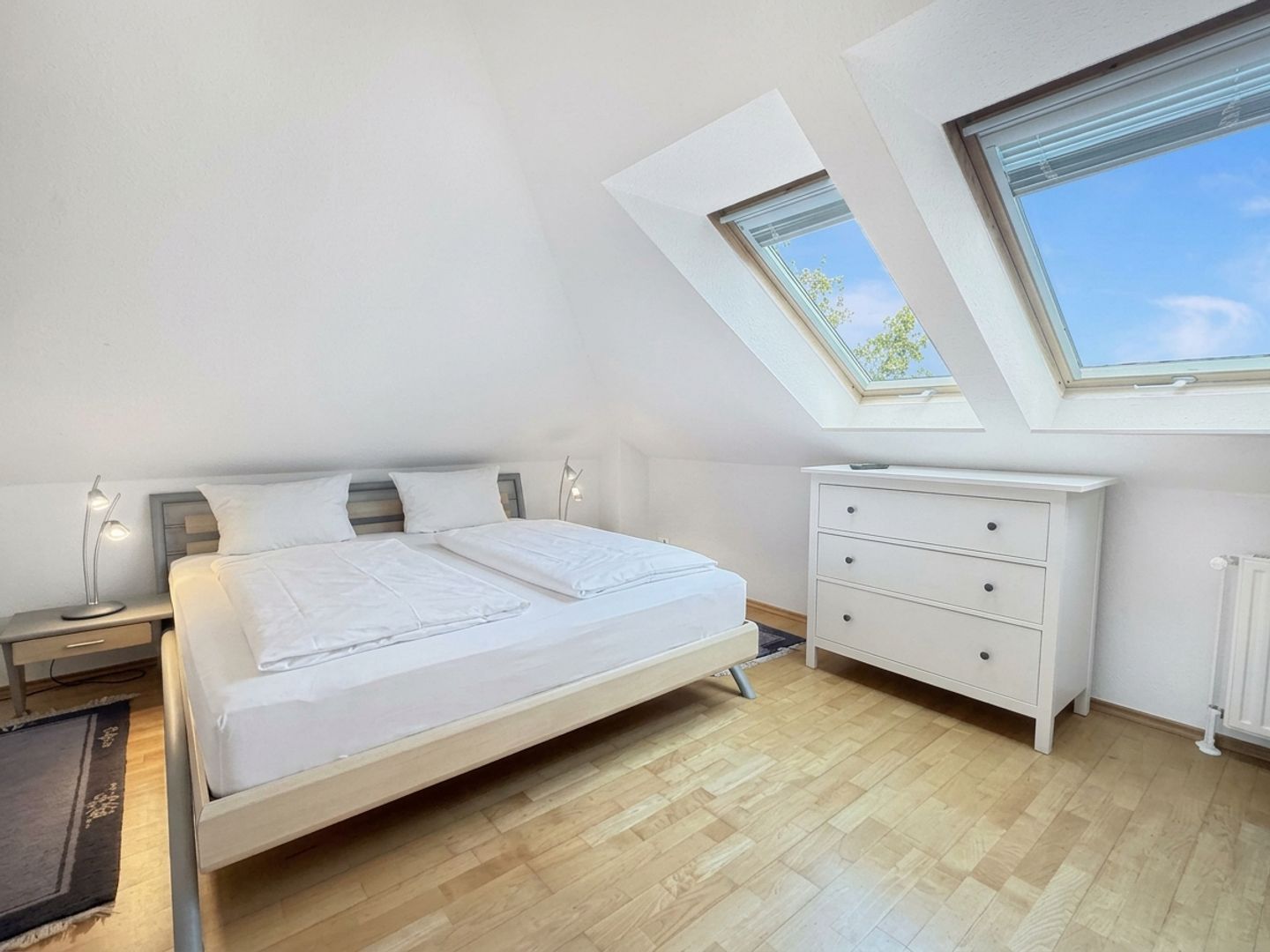 A bedroom with a bed, bedside tables, a dresser, and skylights.