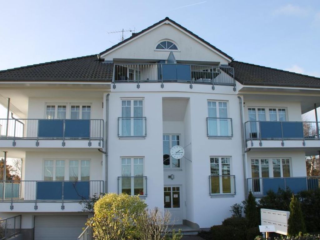 A two-story building with a central entrance, balconies on each floor, and a clock above the door.