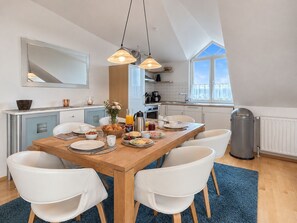 A modern kitchen with a dining table set for breakfast, white chairs, and pendant lighting.