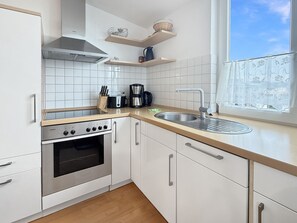 A modern kitchen with white cabinets, a stainless steel oven, a coffee maker, and a window with a view.