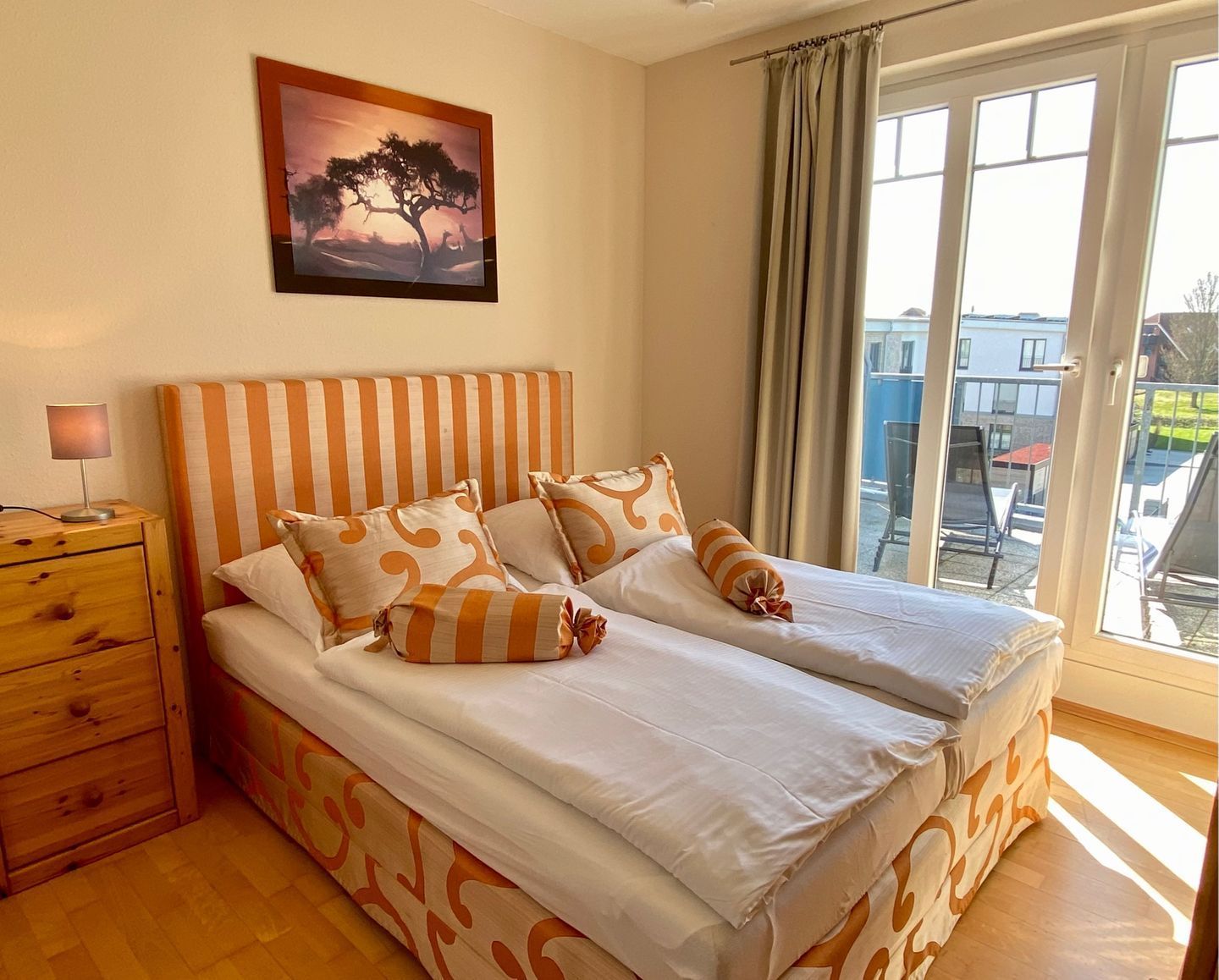 A double bed with striped headboard, a bedside table with a lamp, and a window with curtains.