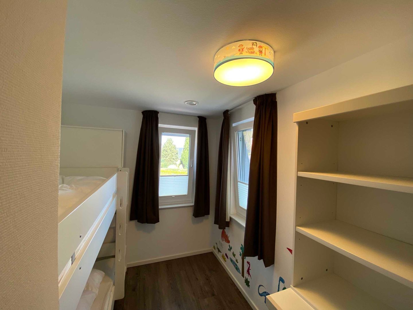 Et værelse med køjeseng, et vindue med gardiner, en loftlampe og en væg med et muralmaleri.