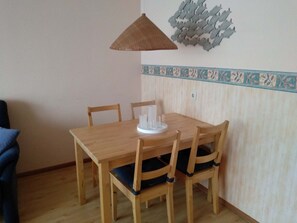 Uma mesa de jantar de madeira com quatro cadeiras, um lustre pendurado e um painel decorativo na parede.