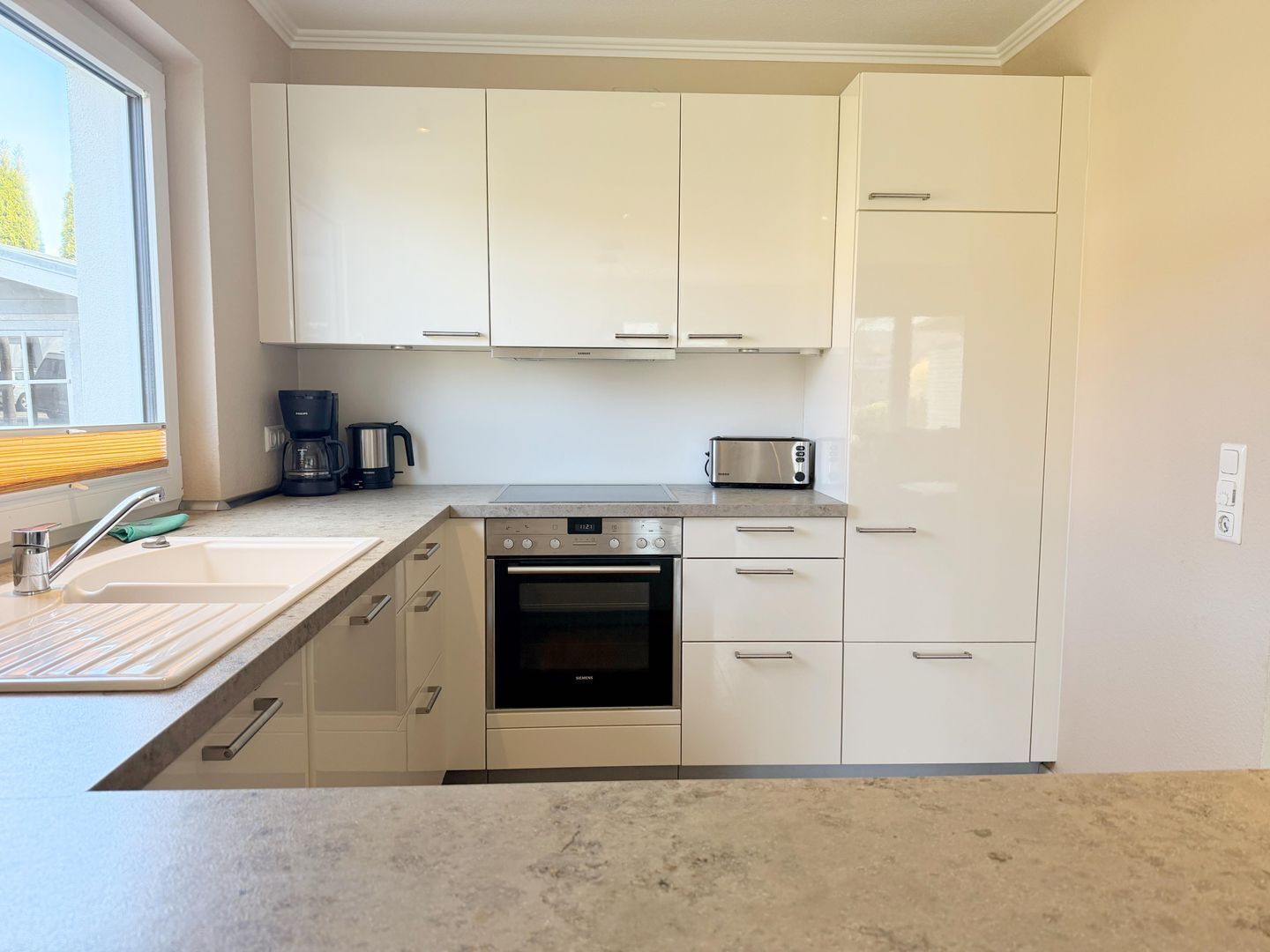 A modern kitchen with white cabinets, a built-in oven, a coffee maker, and a toaster.