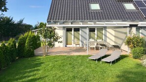 A house with a tiled roof, solar panels, a patio with a table and chairs, and a lawn.
