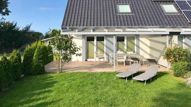Et hus med tegltag, solpaneler, en terrasse med bord og stole, samt en græsplæne.