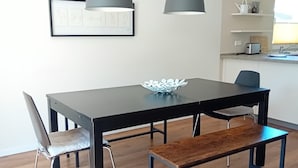 A modern dining area with a black table, two chairs, a bench, and two pendant lights.