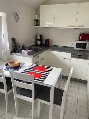 Moderni keittiö, jossa on valkoiset kaapit, mikroaaltouuni, kahvinkeitin ja seinällä oleva kello.