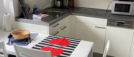 A modern kitchen with white cabinets, a microwave, a coffee maker, and a clock on the wall.