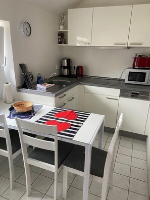 Uma cozinha moderna com armários brancos, micro-ondas, máquina de café e um relógio na parede.
