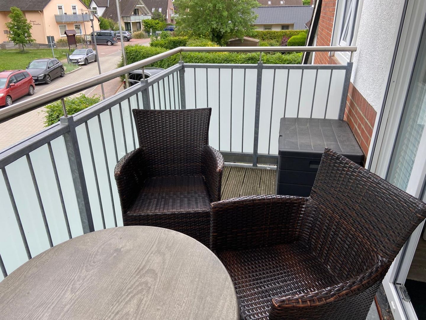 En balkong med flätade stolar och ett bord, med utsikt över ett bostadsområde.