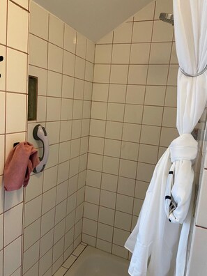 A shower with white tiles, a towel rack with a pink towel, and a white robe hanging on a rack.