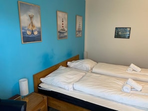 Quarto de hotel com duas camas, cabeceira de madeira, mesa de cabeceira com abajur e três quadros na parede.