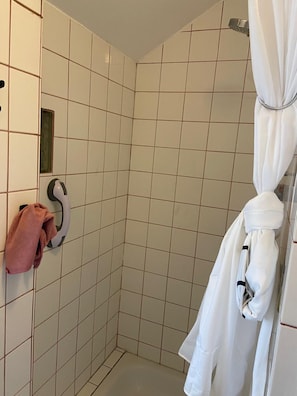 Eine Dusche mit weißen Fliesen, ein Handtuchhalter mit einem rosa Handtuch und ein weißer Bademantel, der an einem Gestell hängt.