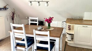A dining area with a wooden table, white chairs, a vase of flowers, and a kitchen area with white cabinets and a wooden countertop. - 7016 "incl. beach chair" - 7016 "incl. beach chair" - An der Aue 9c - Apartment 25 (Dahme)