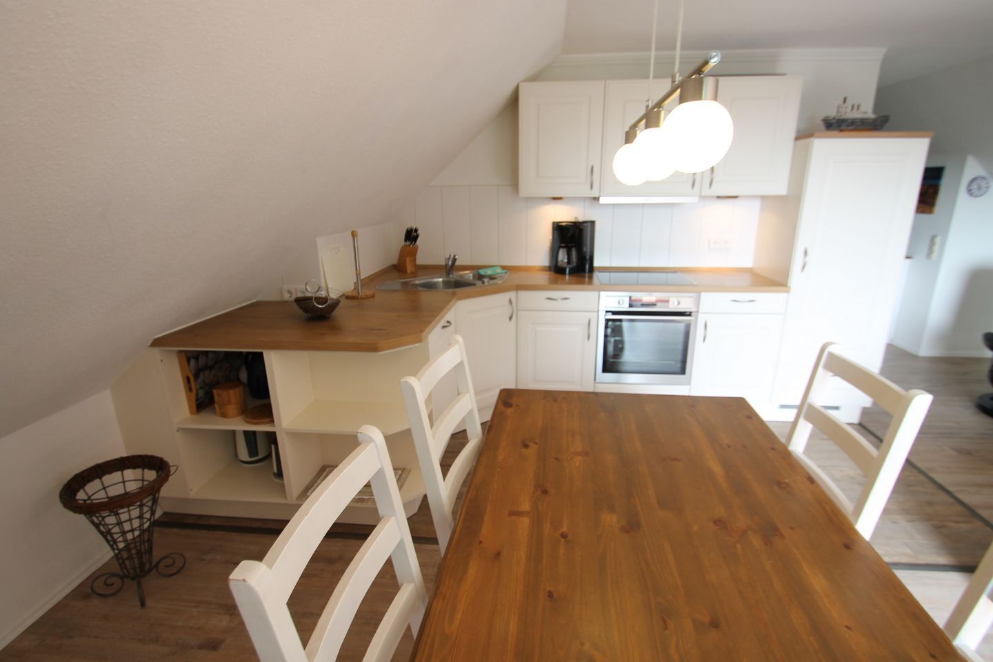 A compact kitchen with white cabinets, a wooden dining table, and a hanging light fixture.
