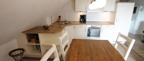 A compact kitchen with white cabinets, a wooden dining table, and a hanging light fixture.